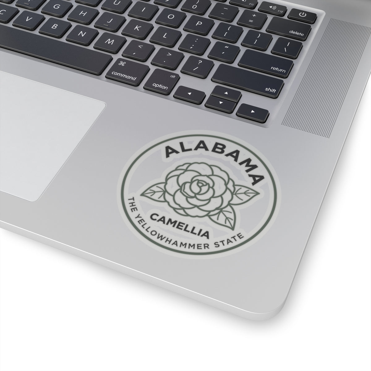 Round Alabama camellia state sticker on silver laptop trackpad area
