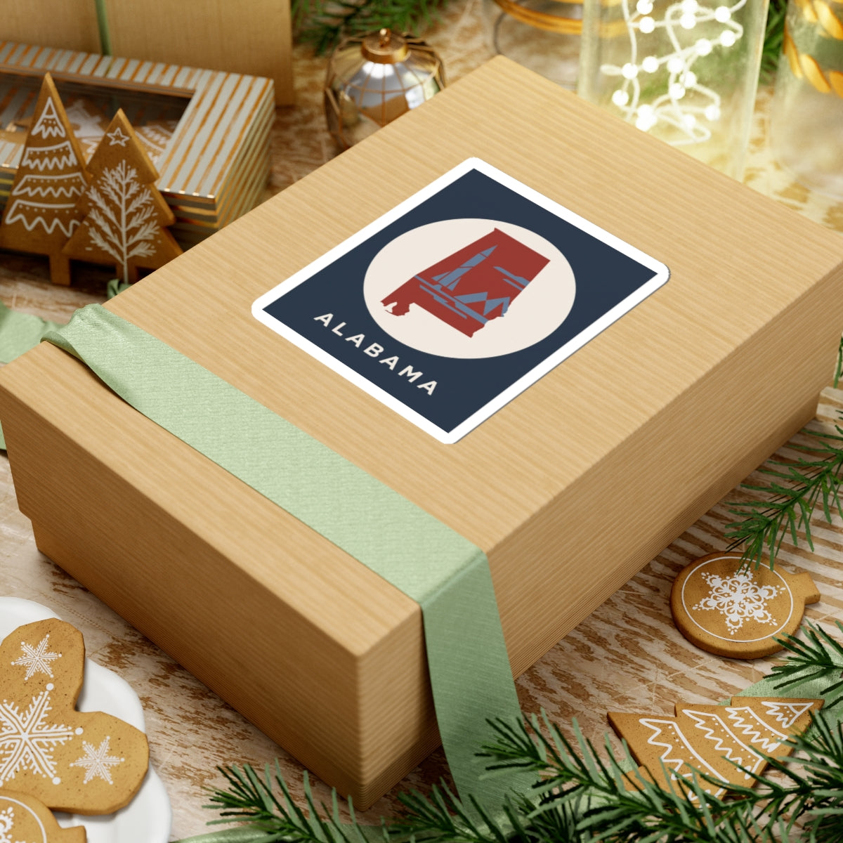 Square Alabama sticker on wrapped gift: red landmark in white circle, navy backing