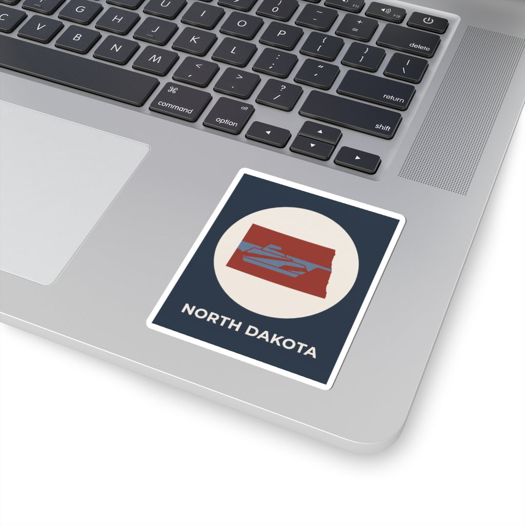 North Dakota map sticker on a laptop lid, navy square with red state icon and text