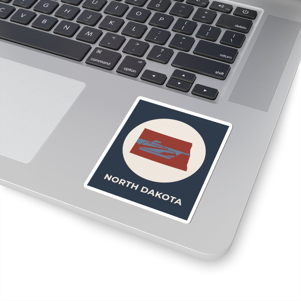 North Dakota map sticker on a laptop lid, navy square with red state icon and text