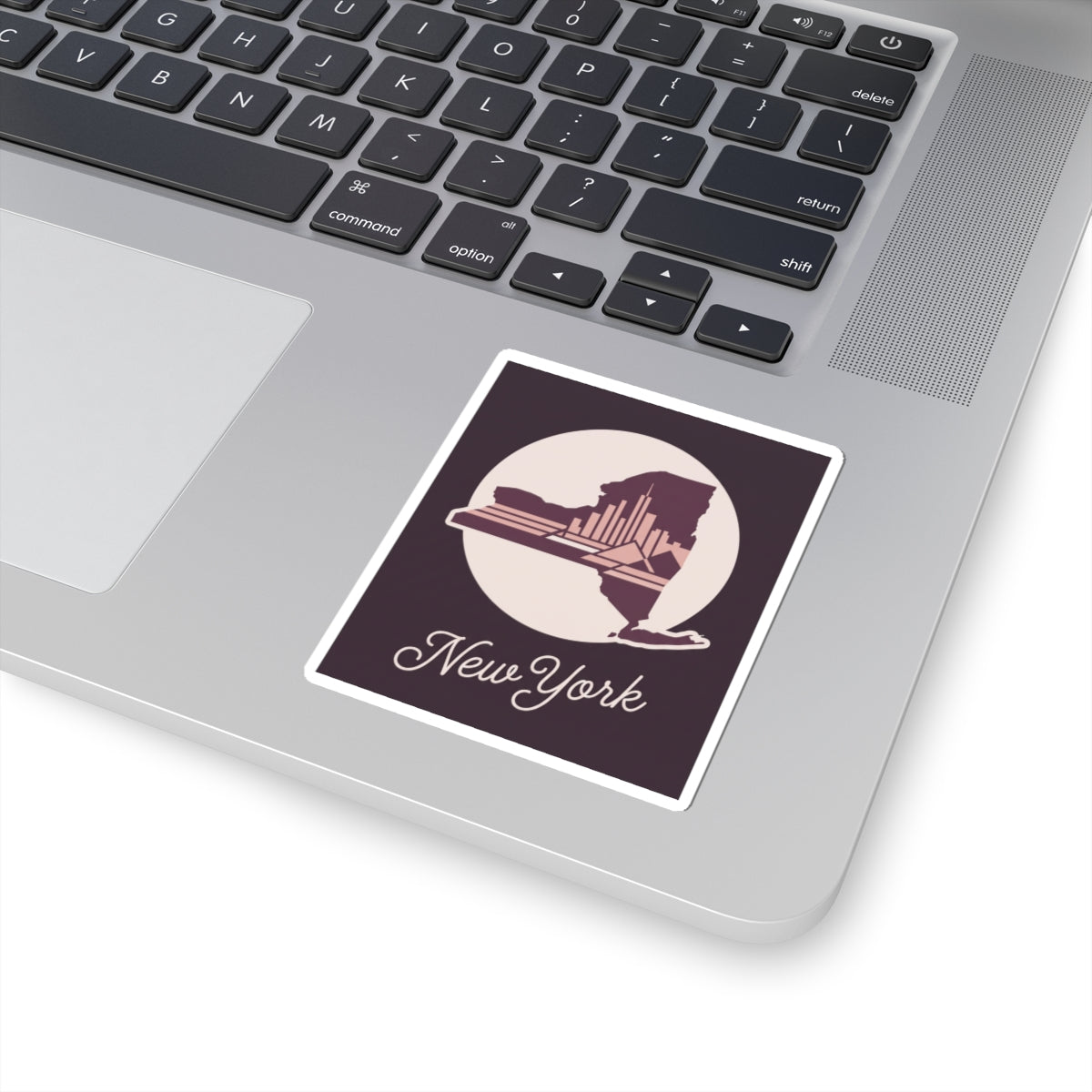 New York skyline decal sticker on a laptop lid, showing circular state silhouette and cursive “New York”.