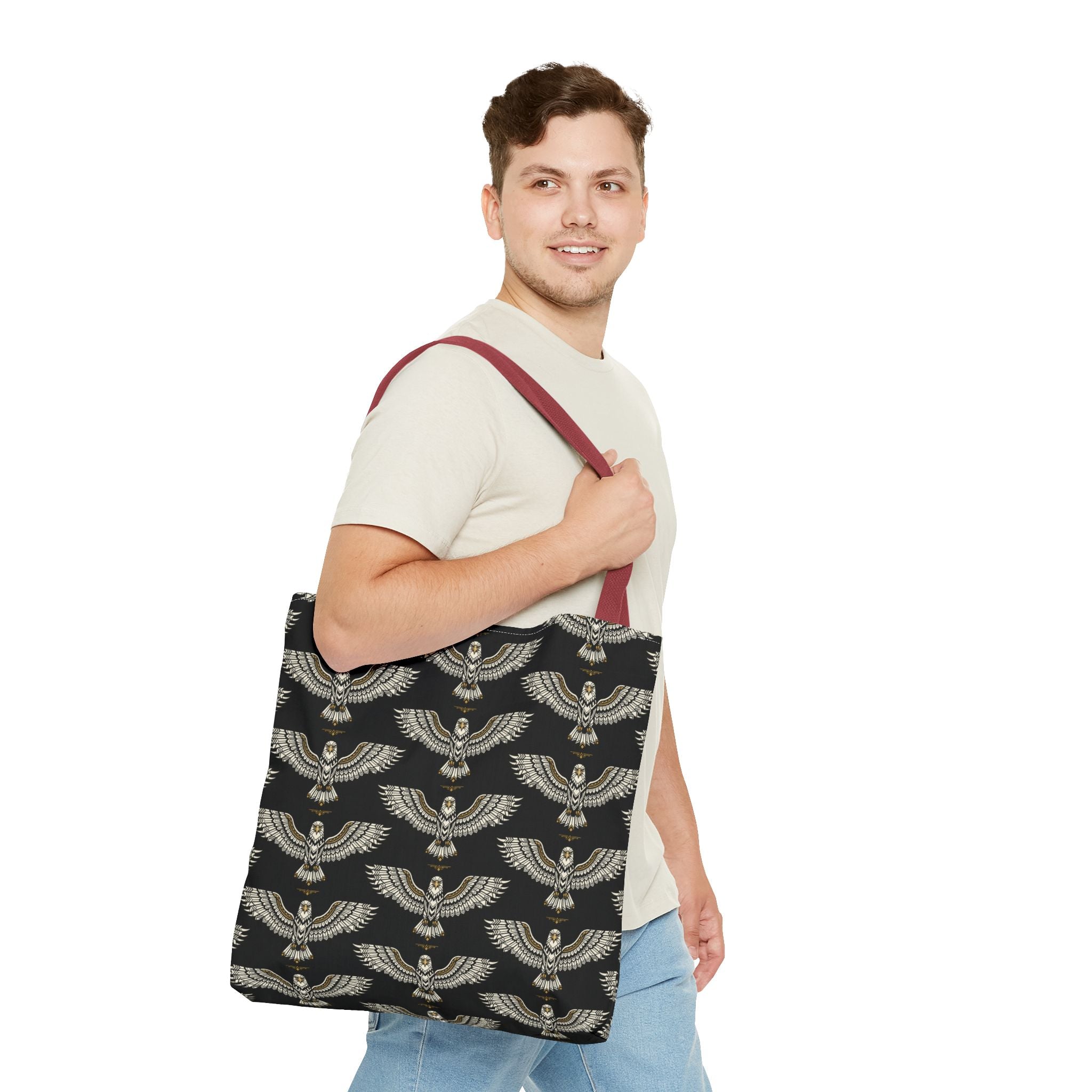 Tote bag held by man: black fabric with gold winged scarab pattern, maroon handles