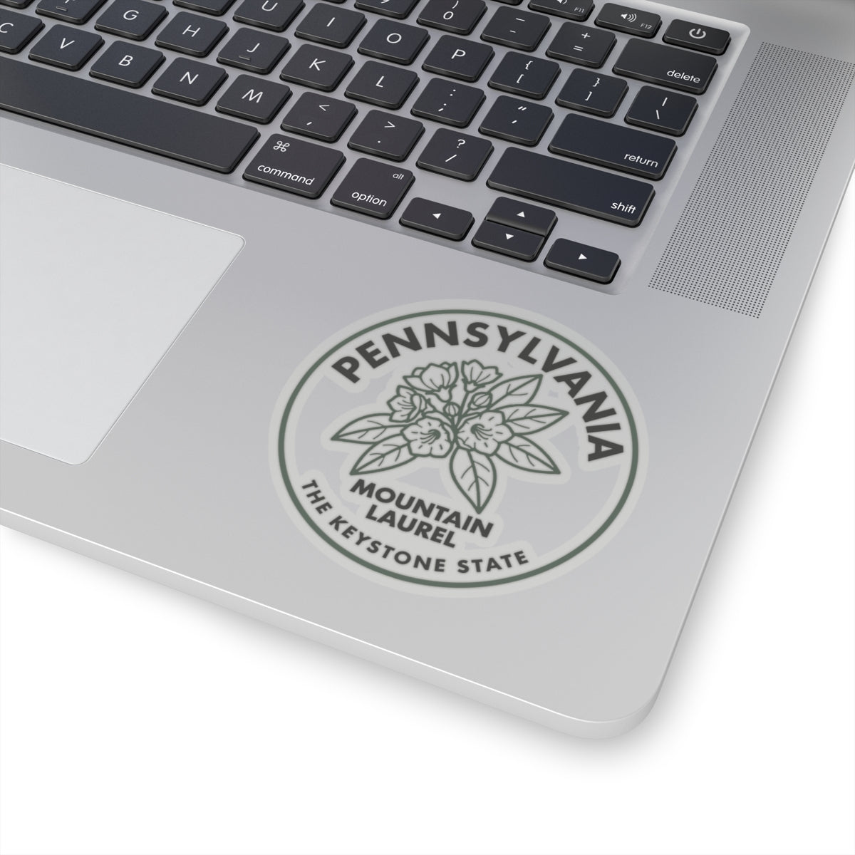 Transparent vinyl sticker on laptop trackpad, circular Pennsylvania Mountain Laurel seal