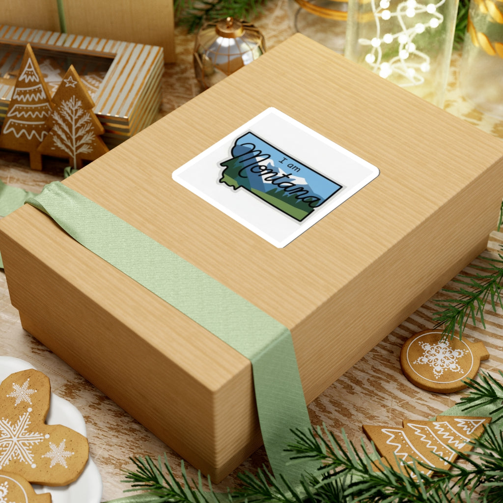 “I am Montana” sticker on gift box, blue sky, green mountains, white outline