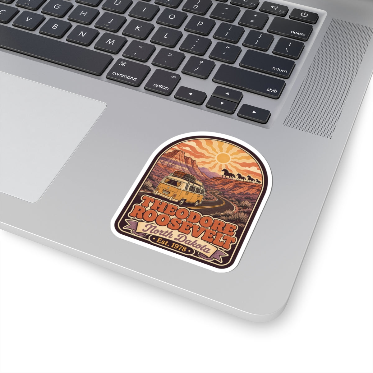 Kiss-cut sticker on a laptop lid, showing camper van desert road and Theodore Roosevelt text