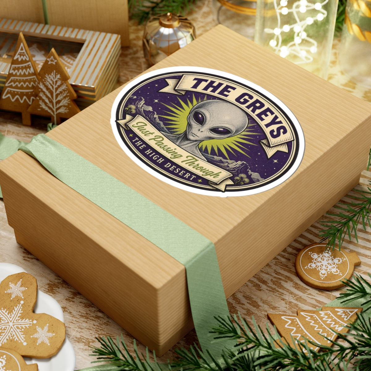 Round alien head sticker on a gift box lid, purple starry art with “THE HIGH DESERT”
