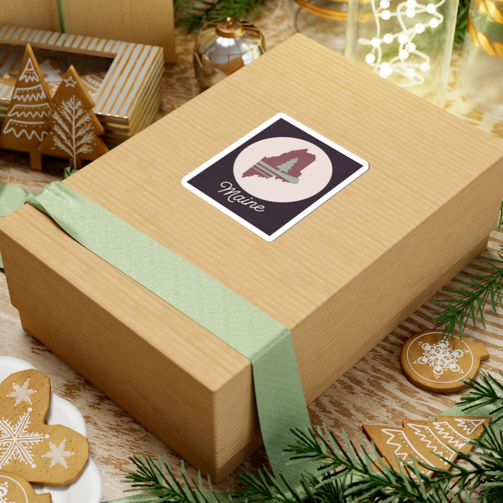 Maine vinyl silhouette sticker on a wrapped gift box, mauve state, pine tree, and 'Maine'.