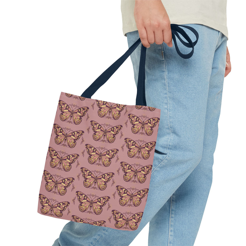 Pink butterfly tote bag with navy handles, held while wearing light denim