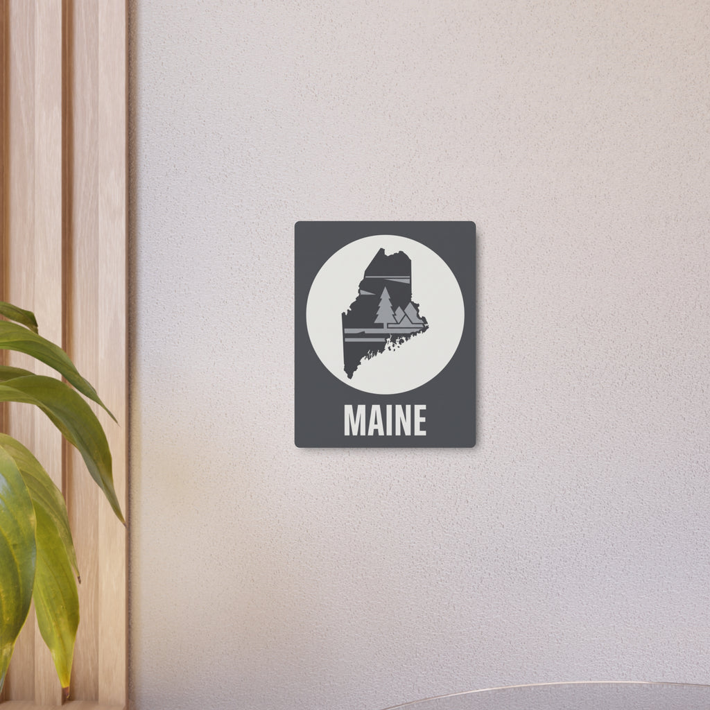 Maine metal art sign on wall: dark gray square, white circle pine silhouette, MAINE lettering