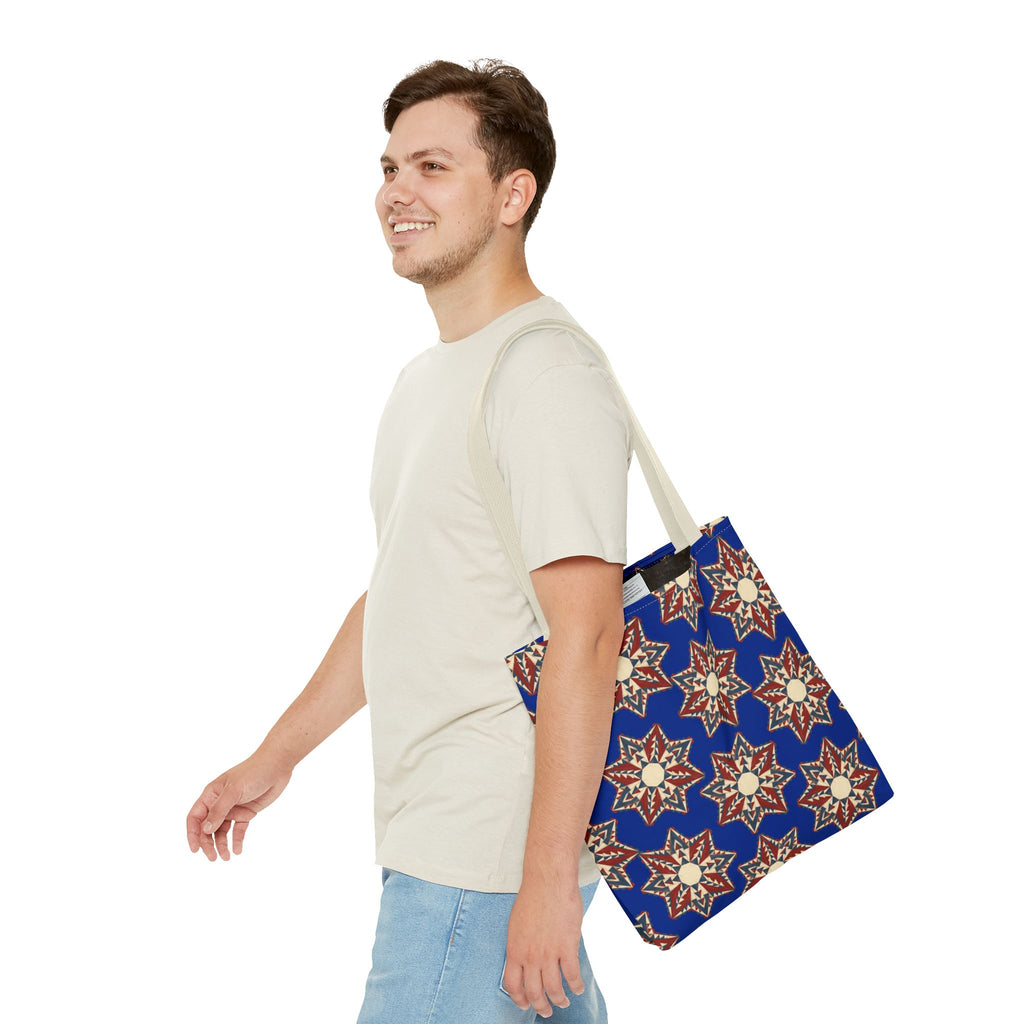 Blue tote bag with starburst floral pattern in cream and red, hanging from light straps